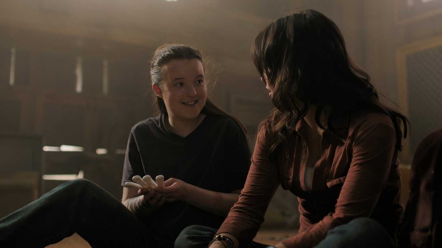 A screengrab from episode 4 of the HBO show The Last of Us Season 2, showing Ellie and Dina smiling at each other.
