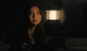A screengrab from episode 4 of the HBO show The Last of Us Season 2, showing Dina holding a lamp while tears stream down her face.