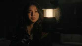 A screengrab from episode 4 of the HBO show The Last of Us Season 2, showing Dina holding a lamp while tears stream down her face.