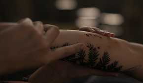 A screengrab from episode 4 of the HBO show The Last of Us Season 2, showing Dina's hands holding Ellie's arm, with a tattoo and bite mark visible on the latter.