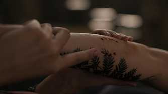A screengrab from episode 4 of the HBO show The Last of Us Season 2, showing Dina's hands holding Ellie's arm, with a tattoo and bite mark visible on the latter.