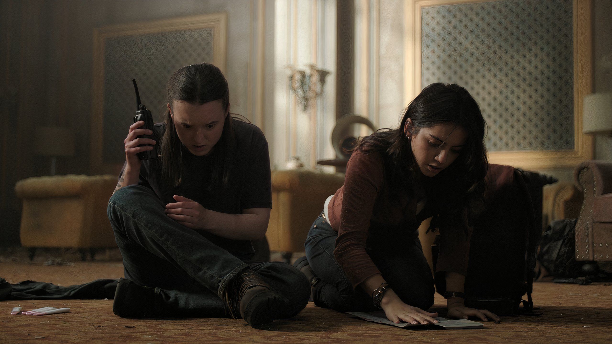 A screengrab from episode 4 of the HBO show The Last of Us Season 2, showing Ellie listening to a walkie-talkie while Dina looks at a map.