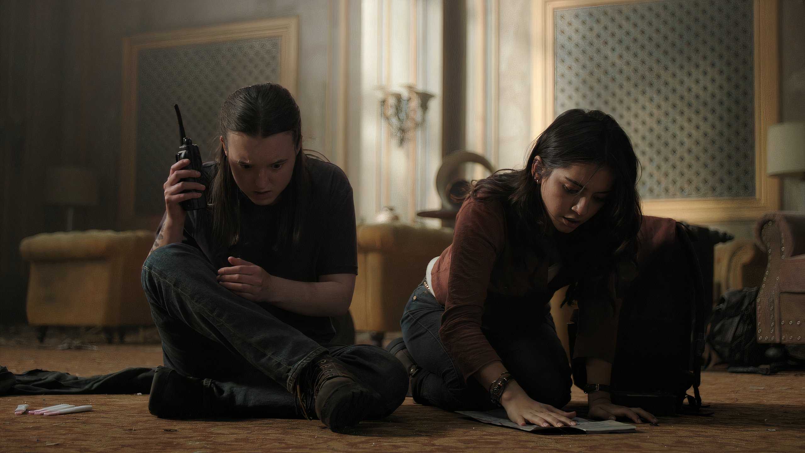A screengrab from episode 4 of the HBO show The Last of Us Season 2, showing Ellie listening to a walkie-talkie while Dina looks at a map.