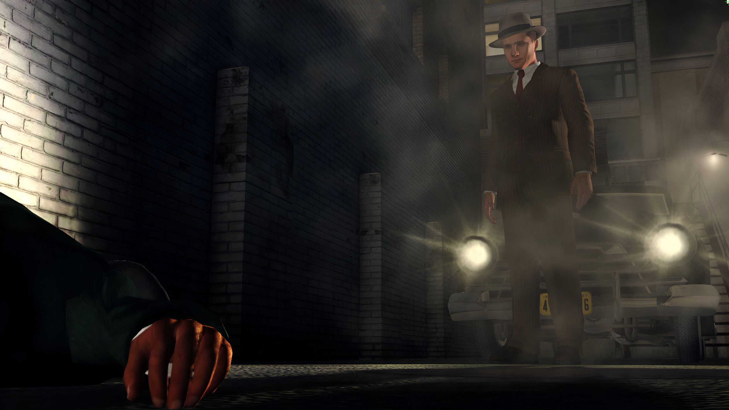 Cole Phelps standing in front of a car with its headlights on in L.A. Noire.