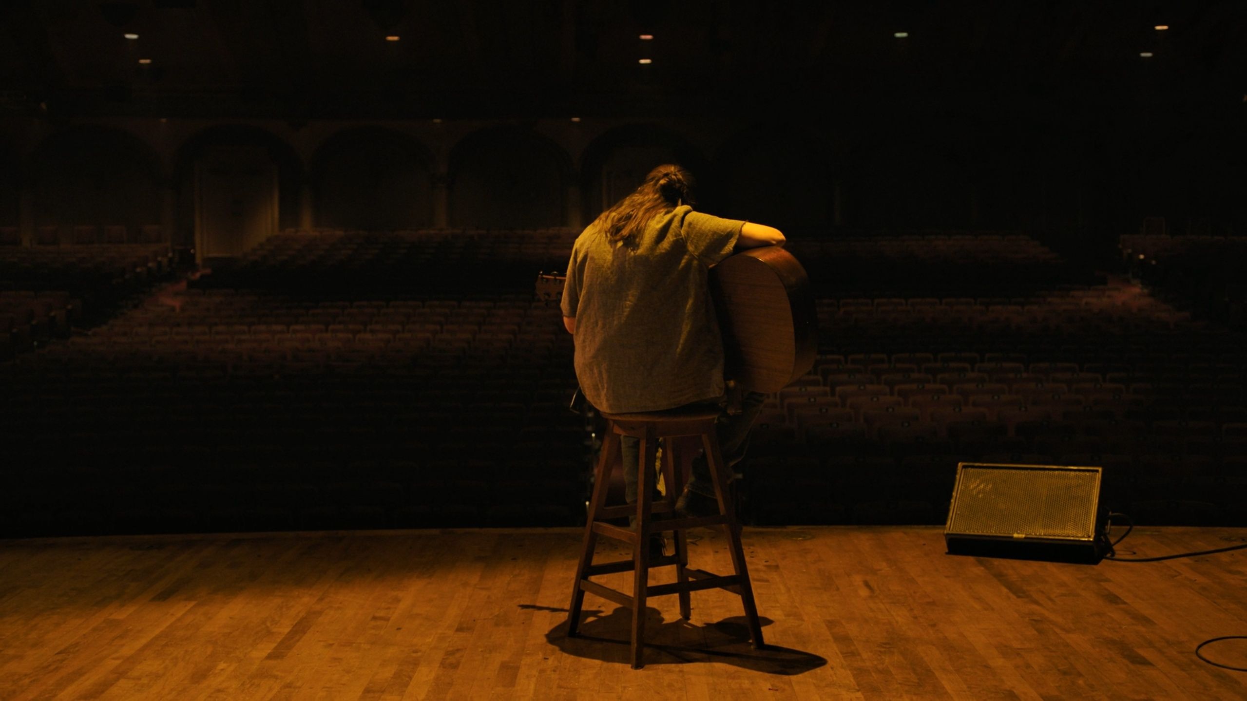 A rear-view shot of Ellie sitting on a stool to play a guitar in HBO's The Last of Us, season 2, episode 5.
