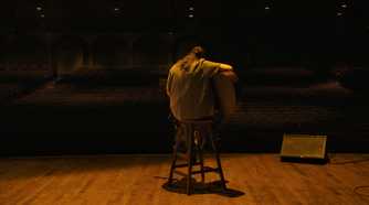 A rear-view shot of Ellie sitting on a stool to play a guitar in HBO's The Last of Us, season 2, episode 5.
