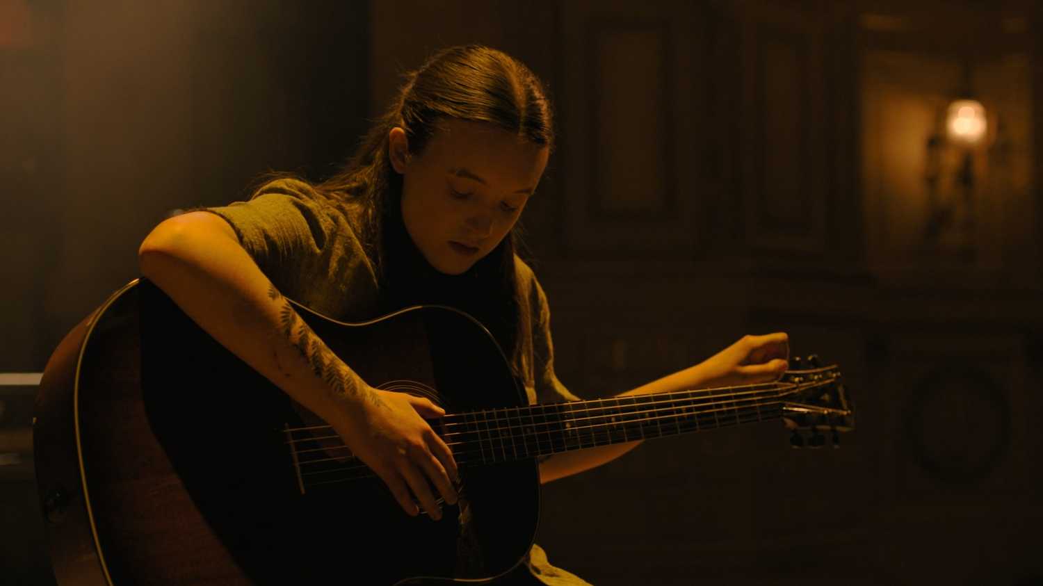 Ellie playing the guitar in HBO's The Last of Us, season 2, episode 5.