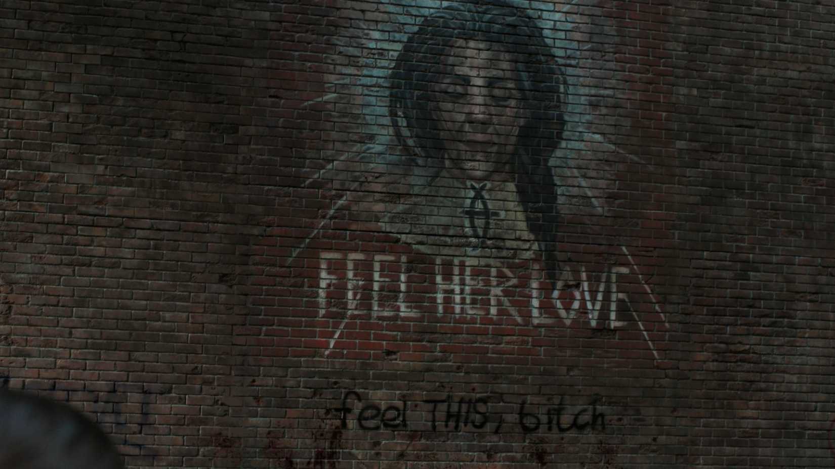 A screengrab from episode 5, season 2 of The Last of Us, showing a mural of a lady's face painted with the words 'Feel Her Love' painted underneath.