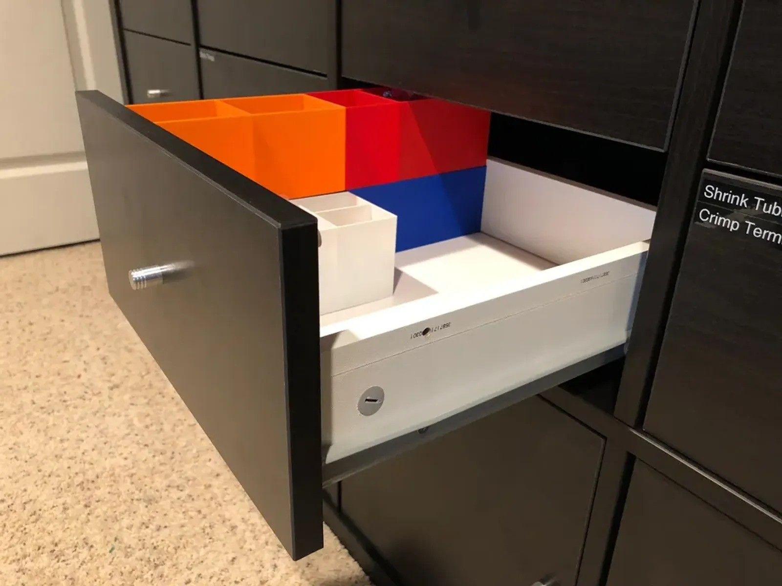 A black IKEA Kallax drawer with colorful 3D printed plastics