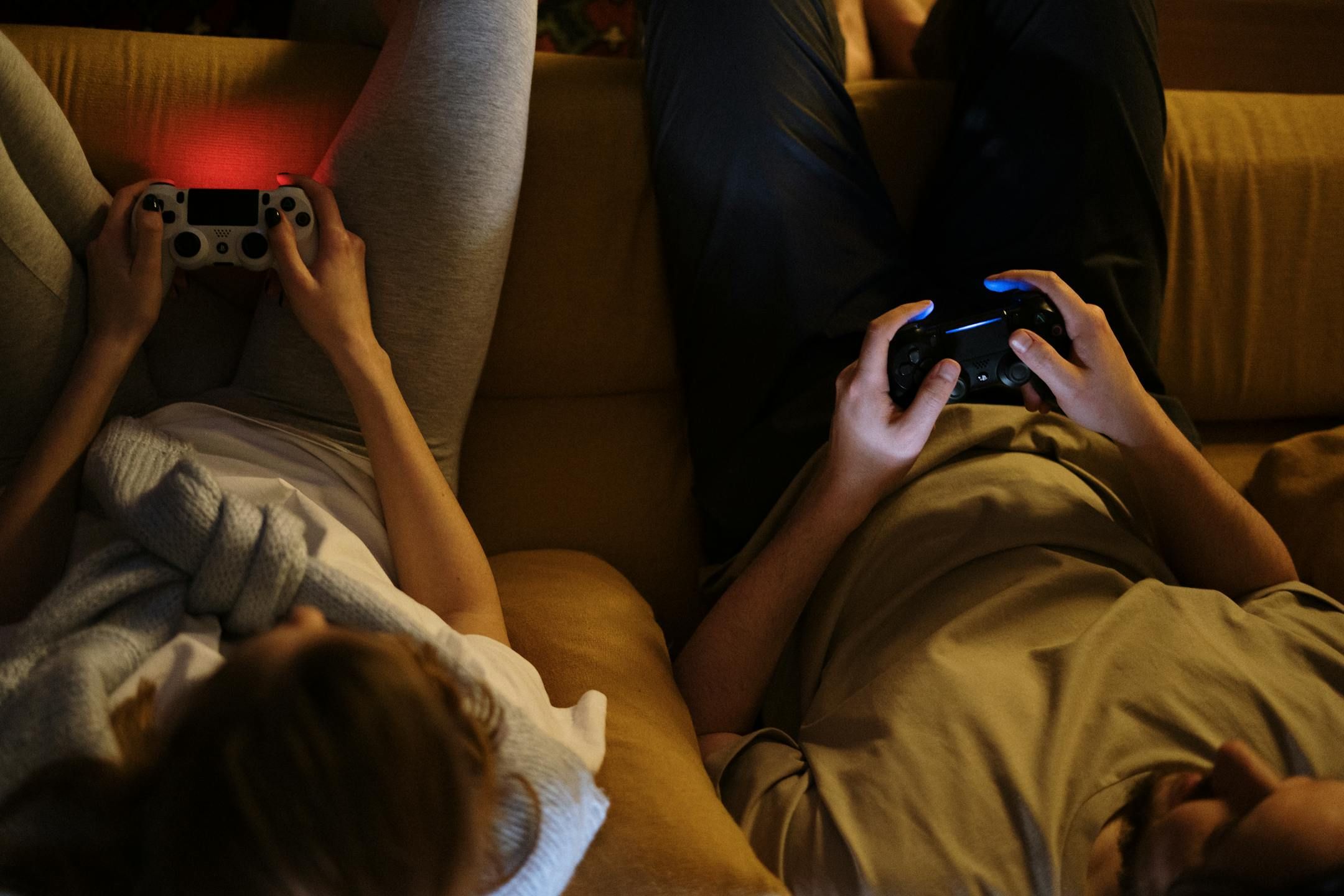 A couple holding PS4 controllers while sitting on a sofa.