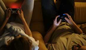 A couple holding PS4 controllers while sitting on a sofa.