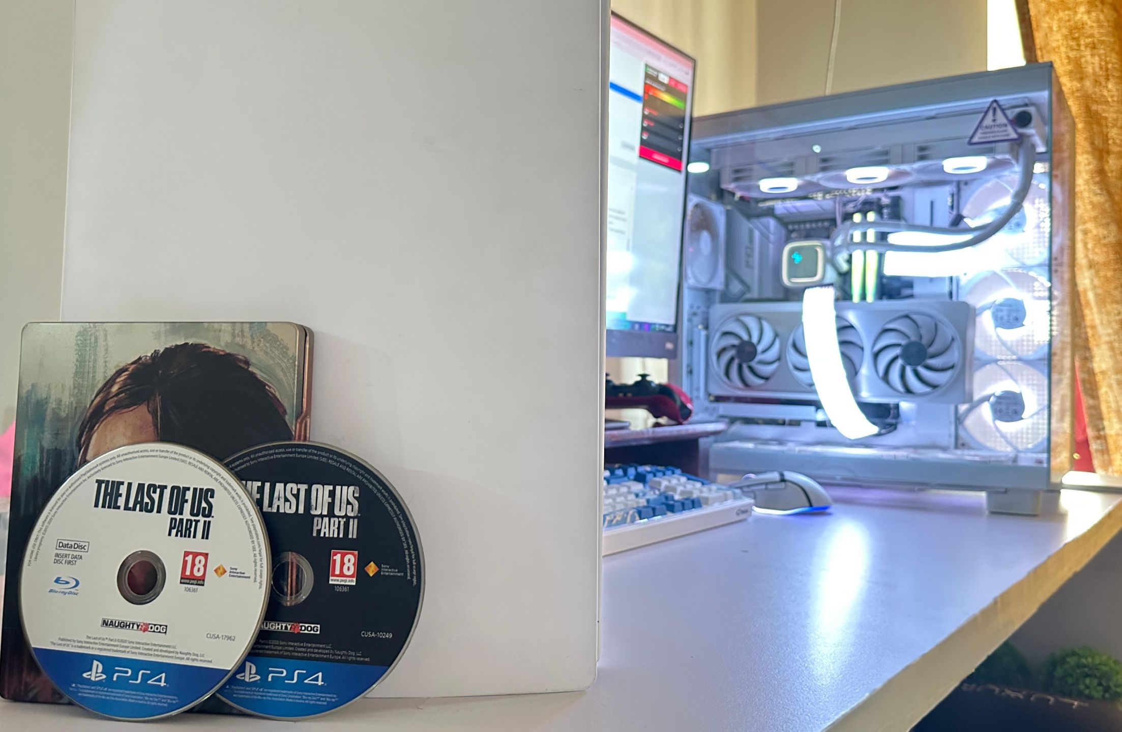 Two discs for The Last of Us Part II PS4 version, next to a PC and a PS5.