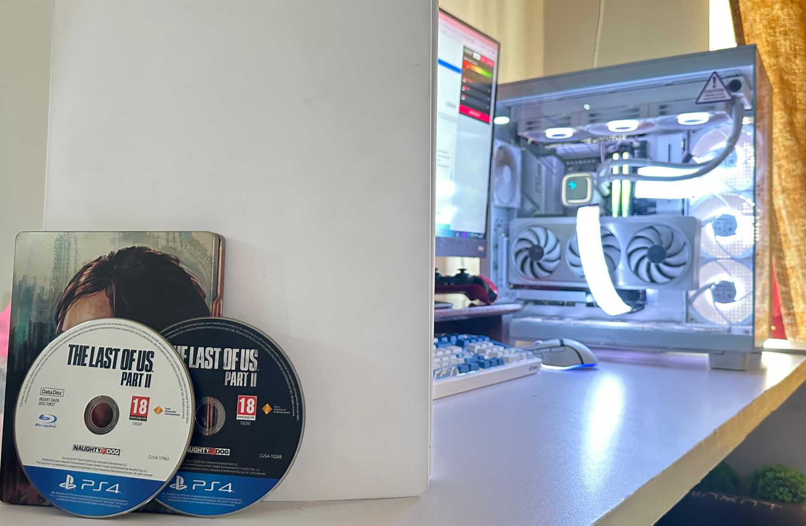 Two discs for The Last of Us Part II PS4 version, next to a PC and a PS5.