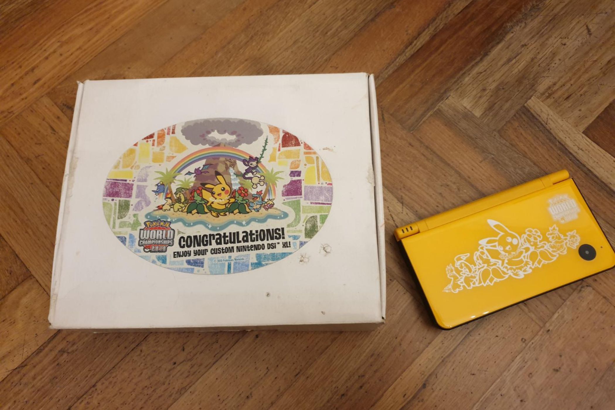 The box and console of a A folded yellow Nintendo DSi XL from the 2010 Pokemon World Championships.