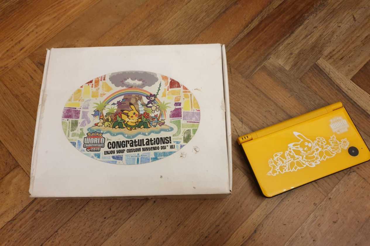 The box and console of a A folded yellow Nintendo DSi XL from the 2010 Pokemon World Championships.