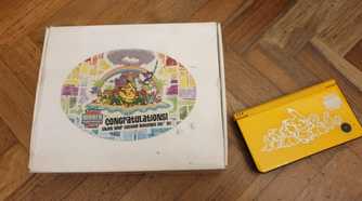 The box and console of a A folded yellow Nintendo DSi XL from the 2010 Pokemon World Championships.