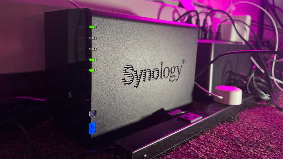 A Synology NAS next to a power strip and UPS on a carpeted floor