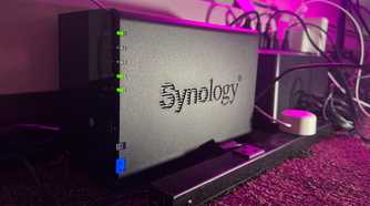 A Synology NAS next to a power strip and UPS on a carpeted floor
