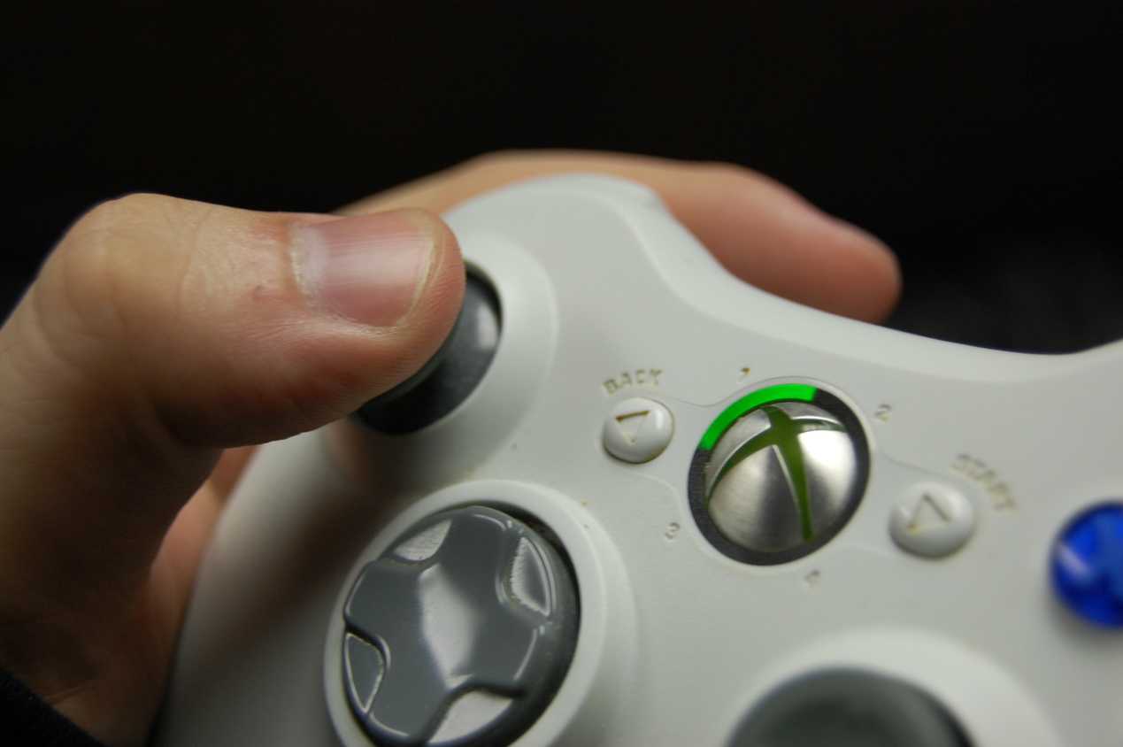 A hand holding an Xbox 360 controller in white.