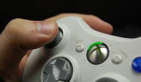 A hand holding an Xbox 360 controller in white.