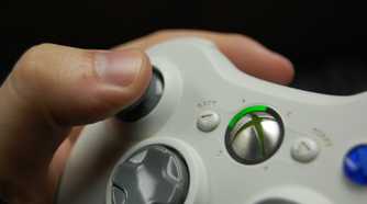 A hand holding an Xbox 360 controller in white.