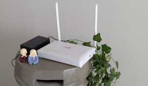 A white router on a stand next to green leaves