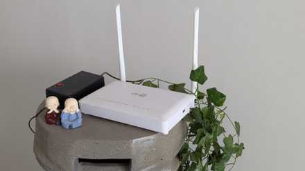 A white router on a stand next to green leaves