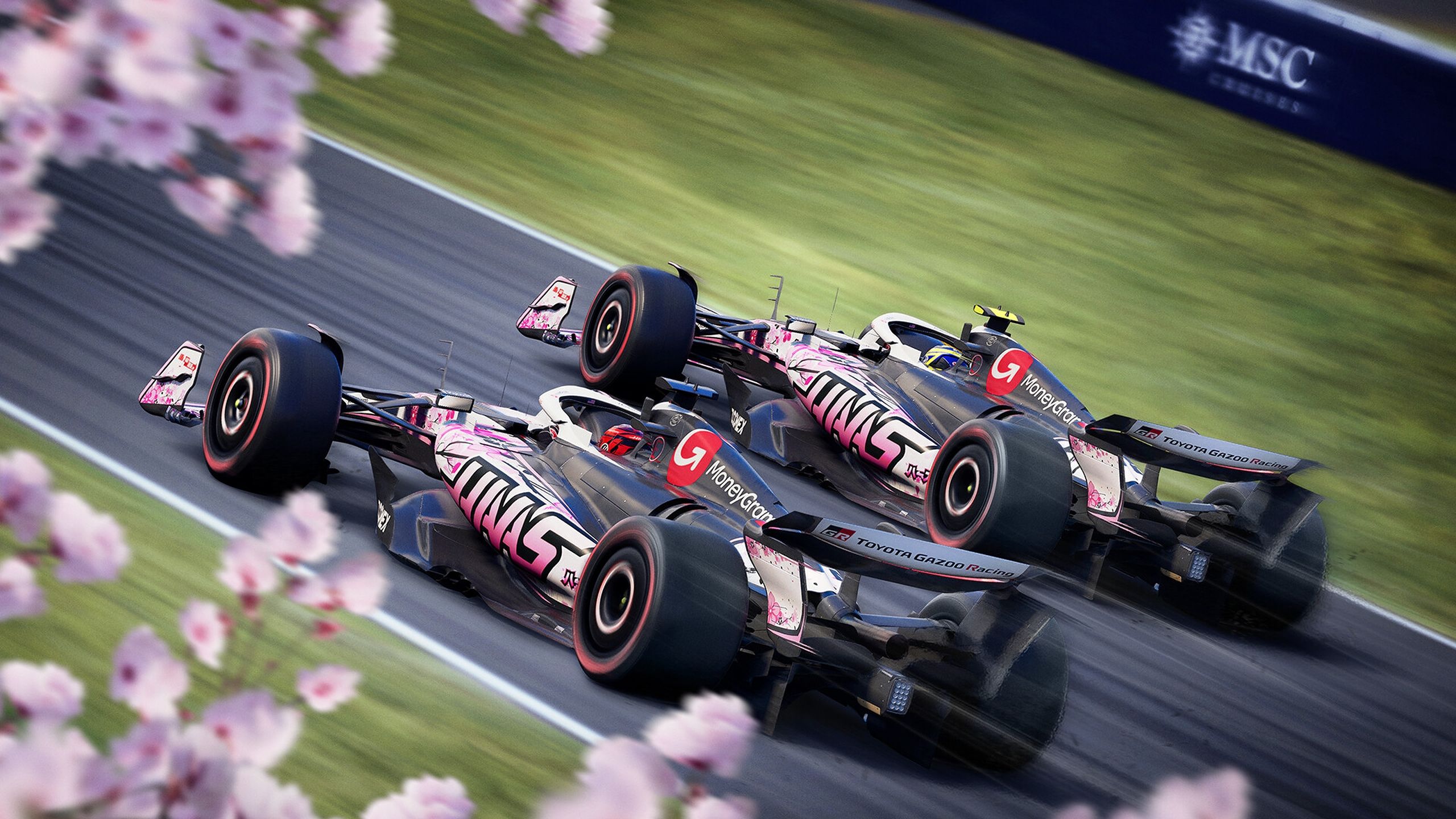 Two Formula 1 cars racing on a track with sakura petals in the foreground.