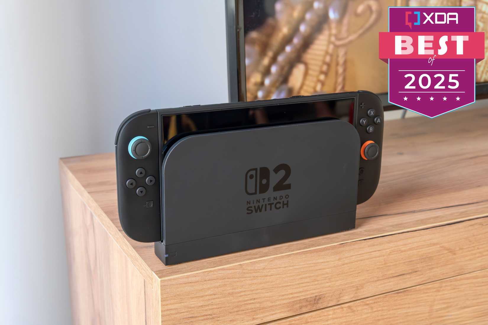 Una Nintendo Switch 2 en su base frente a un televisor. La imagen tiene una lectura de placa. "XDA Lo mejor de 2025" en la esquina superior derecha