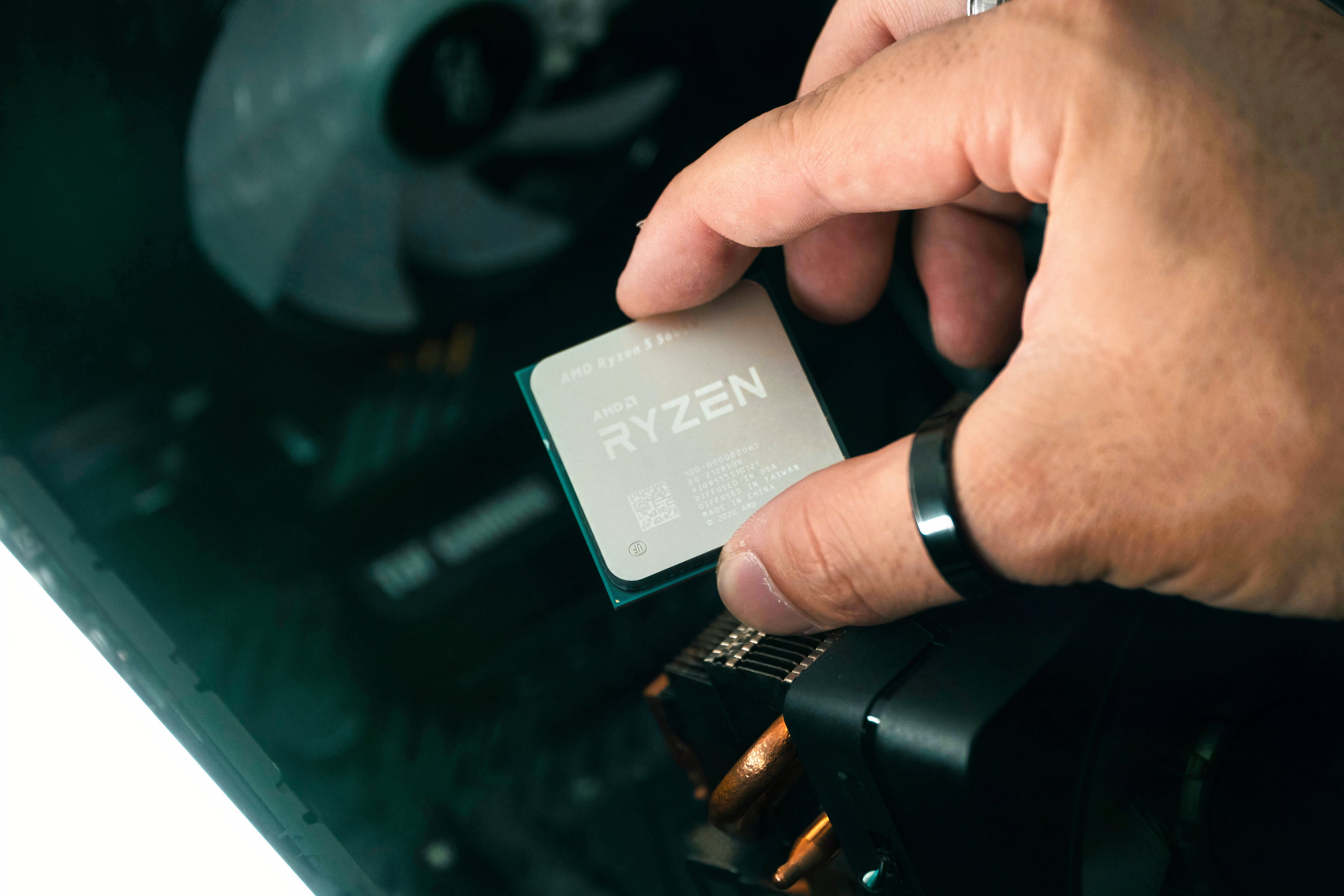 An image of a person holding a Ryzen 5 CPU over a motherboard.