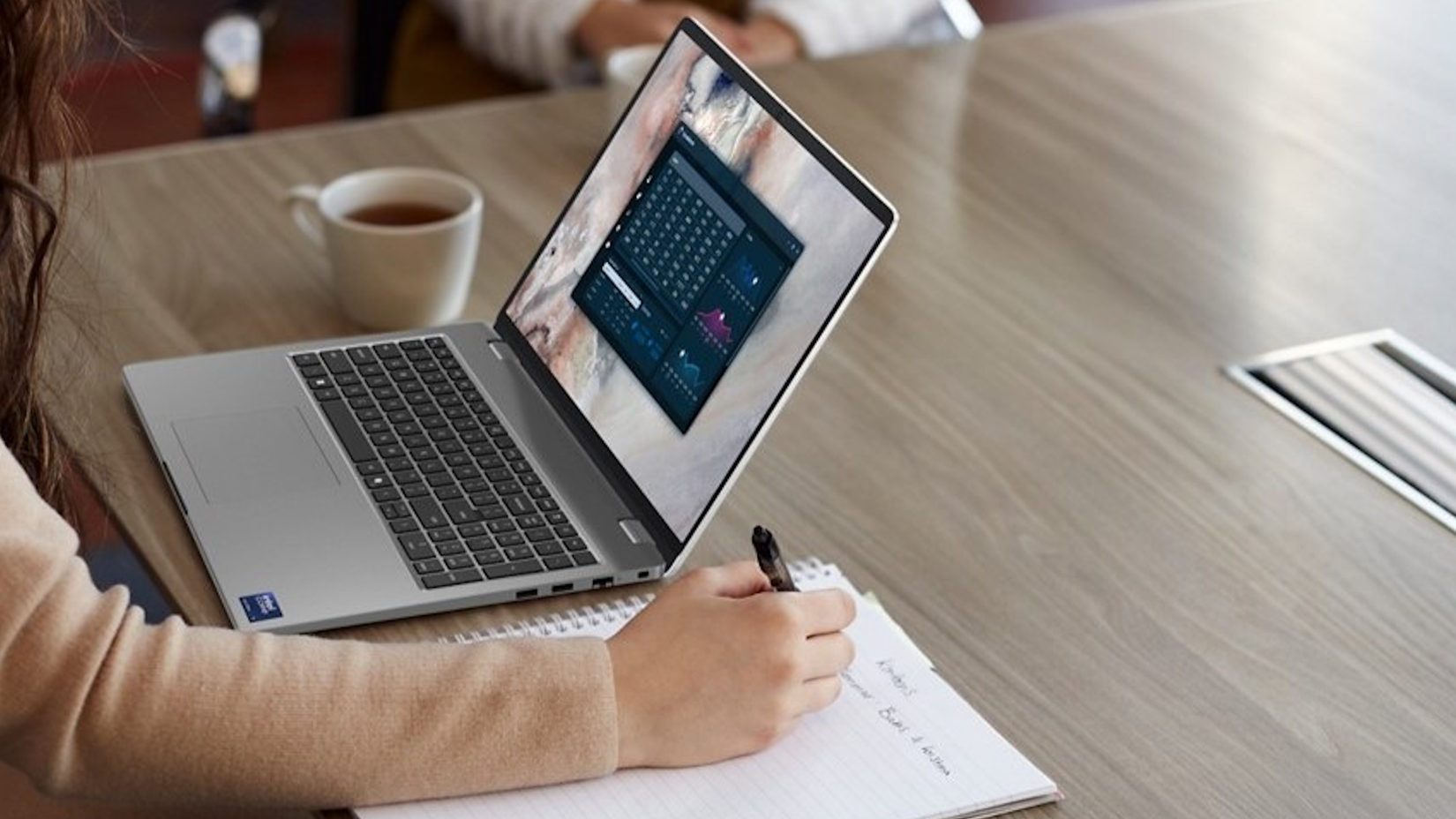 A woman takes notes while worjing on her Dell laptop