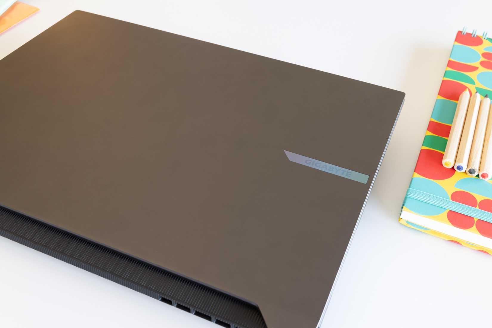 Angle view of a closed GIGABYTE AERO X16 next to a notebook with pencils on top