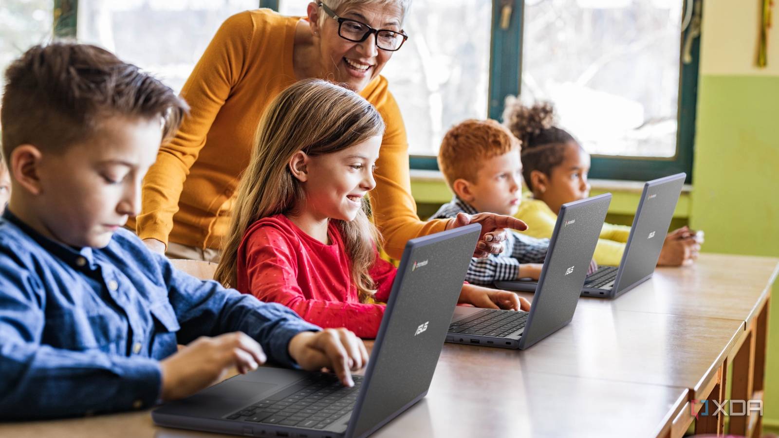 A group of students using Asus Chromebook CR1102 laptops in a classroom with a teacher giving them instructions