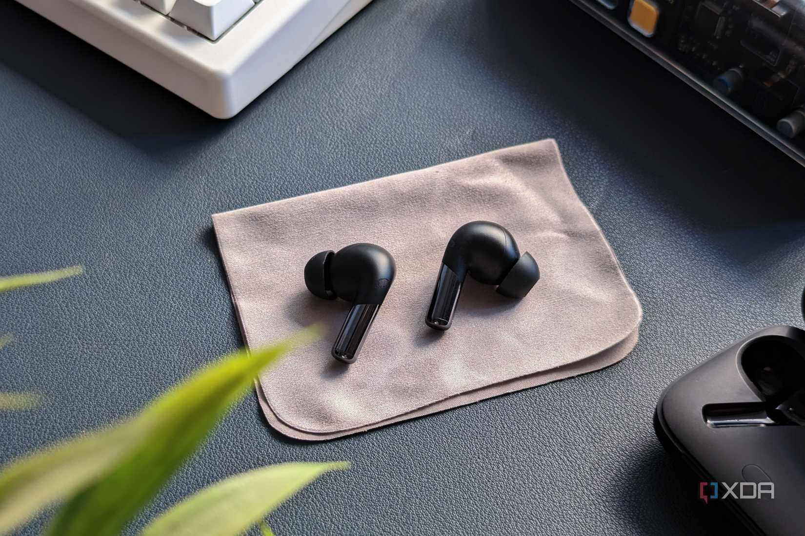 OnePlus Buds Pro 2 colocado sobre un paño de microfibra sobre un fondo azul con su estuche de carga, un teclado y una planta en el marco.