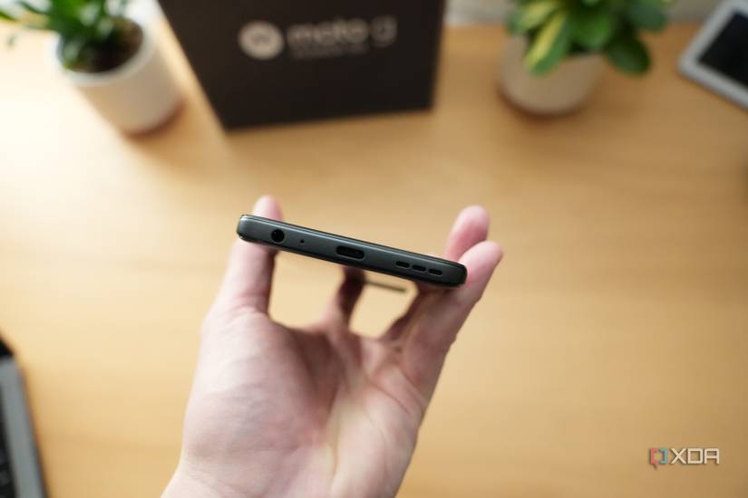 Motorola G Power 5G 2023 bottom showing USB-C port, 3.5mm jack, and speaker in front of wood desk with plants and phone's packaging in background