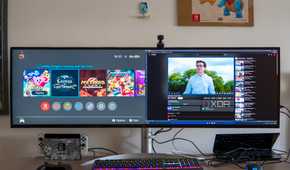 A desk with an LG UltraWide 49W95C monitor connected to a laptop and a Nintendo Switch, both of which are displaying on the monitor simultaneously.