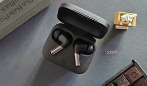 An image showing a pair of OnePlus Buds Pro 2 earbuds kept in the charging box next to its retail box, a keyboard, and an artisan keycap.
