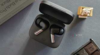 An image showing a pair of OnePlus Buds Pro 2 earbuds kept in the charging box next to its retail box, a keyboard, and an artisan keycap.