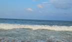 A image showing a beach-side view with bright blue sky, lots of water, and sand.
