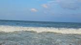 A image showing a beach-side view with bright blue sky, lots of water, and sand.