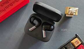 An image showing a pair of OnePlus Buds Pro 2 earbuds kept in the charging box next to its retail box, a keyboard, and an artisan keycap.