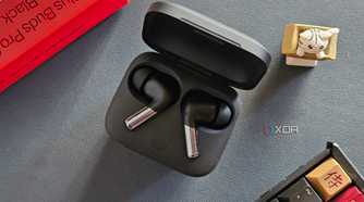 An image showing a pair of OnePlus Buds Pro 2 earbuds kept in the charging box next to its retail box, a keyboard, and an artisan keycap.