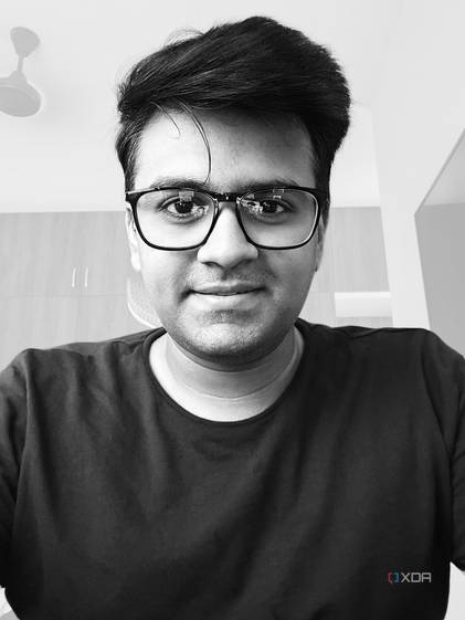 A monochrome selfie of a man with wooden wardrobe and a ceiling fan in the background.
