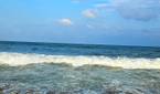 A image showing a beach-side view with bright blue sky, lots of water, and sand.