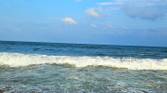 A image showing a beach-side view with bright blue sky, lots of water, and sand.