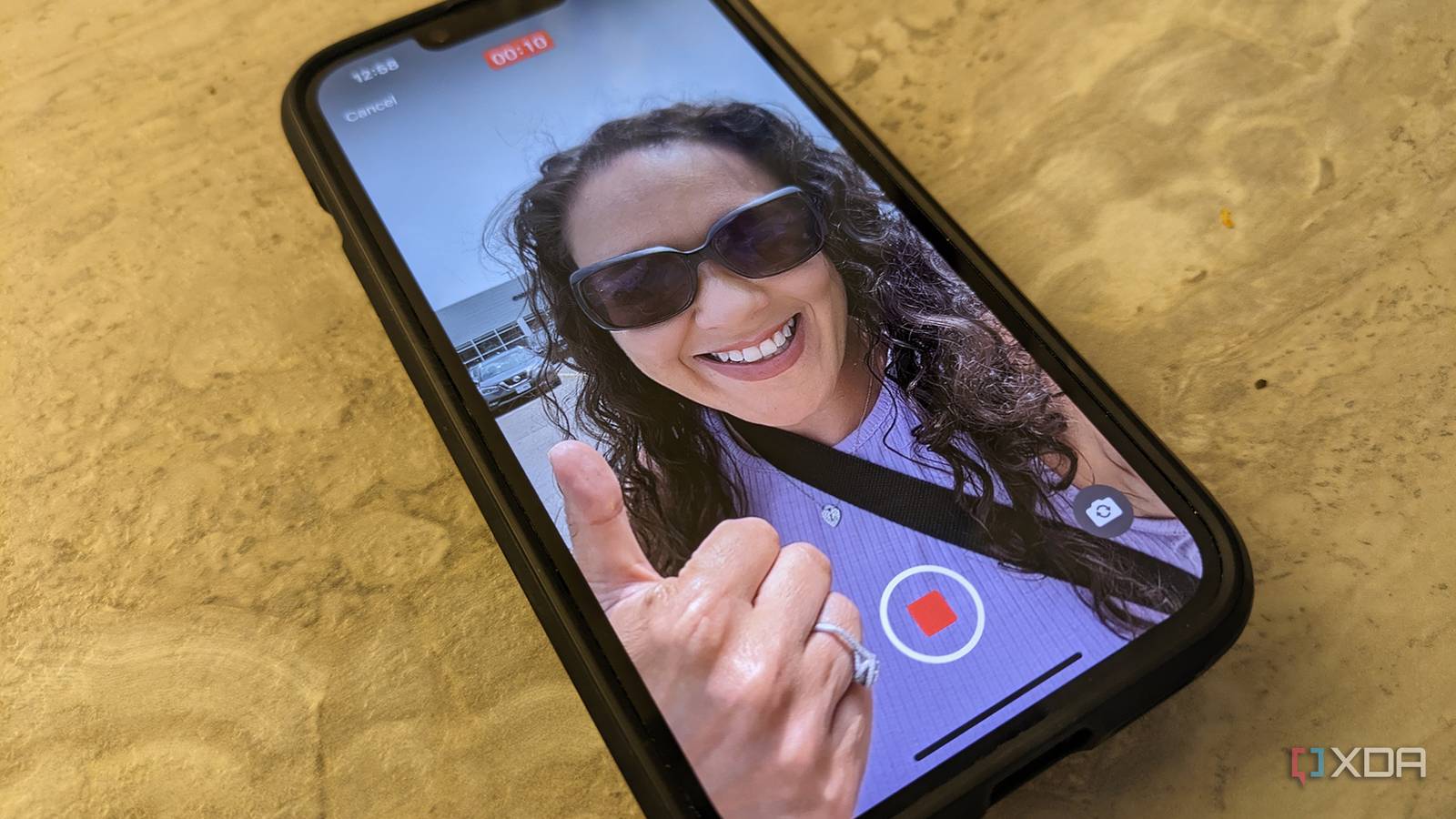 An iPhone 14 on a counter with the image of a woman giving a thumbs up on screen, a record button at the bottom.