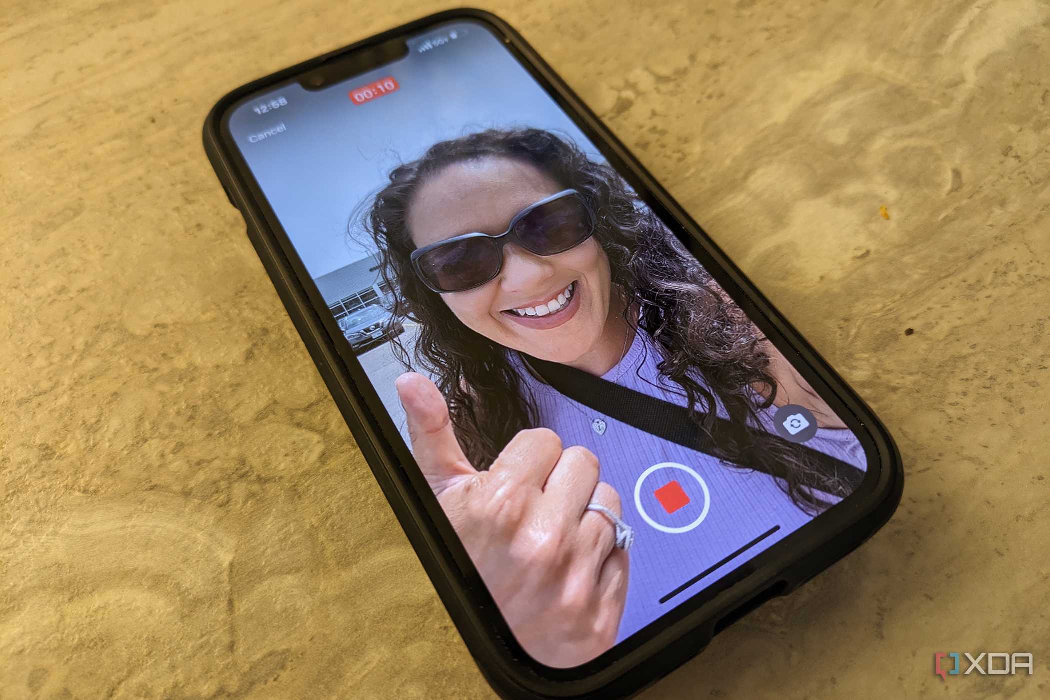 An iPhone 14 on a counter with the image of a woman giving a thumbs up on screen, a record button at the bottom.