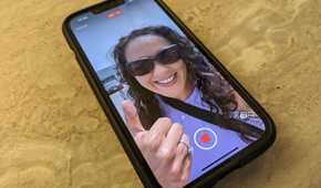 An iPhone 14 on a counter with the image of a woman giving a thumbs up on screen, a record button at the bottom.