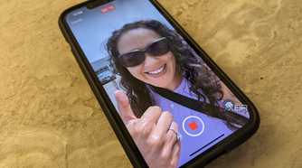 An iPhone 14 on a counter with the image of a woman giving a thumbs up on screen, a record button at the bottom.