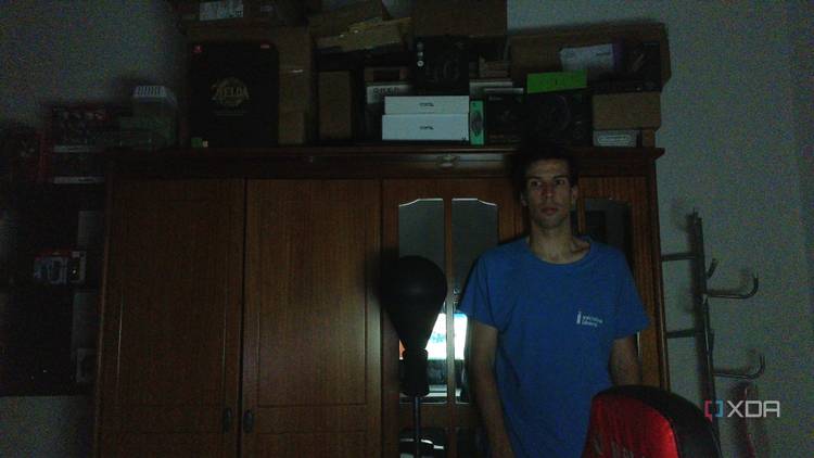 A man standing in a dark room in front of a wardrobe. He's slightly to the left in the frame because the webcam wasn't able to track his position in the dark